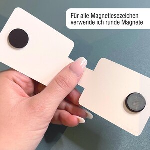 Ein magnetisches Lesezeichen wird aufgeklappt in einer Hand gehalten, so dass man die beiden runden Magnete auf der Innenseite erkennen kann. Im oberen Eck steht der Text: Für alle Magnetlesezeichen verwende ich runde Magnete.