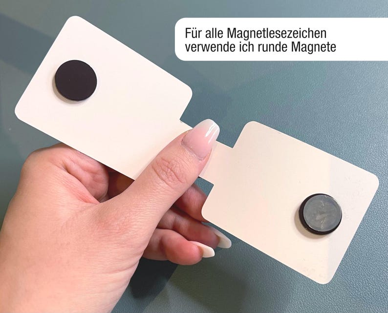 Ein magnetisches Lesezeichen wird aufgeklappt in einer Hand gehalten, so dass man die beiden runden Magnete auf der Innenseite erkennen kann. Im oberen Eck steht der Text: Für alle Magnetlesezeichen verwende ich runde Magnete.