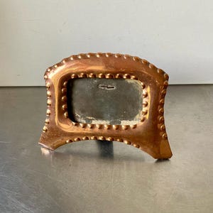 Peut inclure: Un cadre photo en cuivre avec un bord perlé et une ouverture rectangulaire pour une photo. Le cadre a une patine foncée et est légèrement terni.