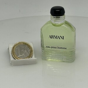 Puede incluir: Una botella de vidrio transparente de Armani Eau de Toilette para hombre. La botella tiene una tapa negra y una etiqueta que dice "ARMANI eau pour homme".