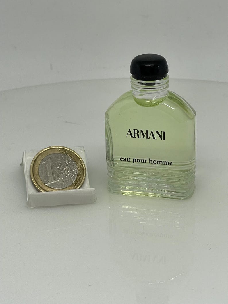 Puede incluir: Una botella de vidrio transparente de Armani Eau de Toilette para hombre. La botella tiene una tapa negra y una etiqueta que dice "ARMANI eau pour homme".