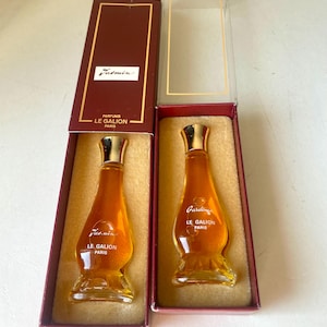 May include: Two miniature perfume bottles in their original boxes. The bottles are clear glass with gold tops and contain a yellow liquid. The boxes are red with gold lettering. The text on the boxes reads "Parfums Le Galion Paris".