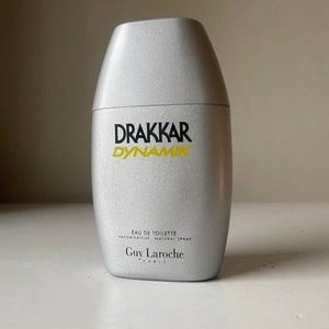 May include: A silver bottle of Drakkar Dynamik Eau de Toilette by Guy Laroche Paris. The bottle has a silver cap and a black and yellow label.