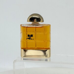 Peut inclure: Un petit flacon de parfum carr&eacute; avec un bouchon et une base dor&eacute;s. La bouteille est de couleur ambre chaud et pr&eacute;sente un motif quadrill&eacute; sur le devant. Un logo noir est visible sur le devant.
