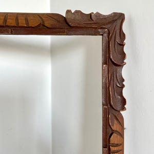 Puede incluir: Un marco de fotos de madera con un diseño tallado y ornamentado. El marco es de color marrón oscuro y tiene una forma rectangular.