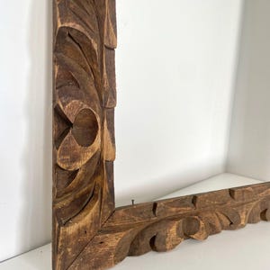 Op de afbeelding: Een donkerbruin houten fotolijst met ingewikkelde houtsnijwerk. De lijst is rechthoekig en heeft een decoratief ontwerp.