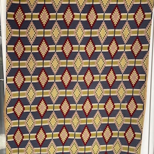 May include: A vintage tapestry with a geometric pattern of diamonds in shades of red, yellow, pink, and blue. The tapestry has a fringe border.