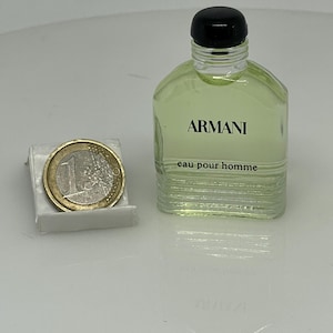 Puede incluir: Un peque&ntilde;o frasco de vidrio transparente de Armani Eau de Toilette para hombre. El frasco tiene una tapa negra y una etiqueta que dice "Armani eau pour homme".