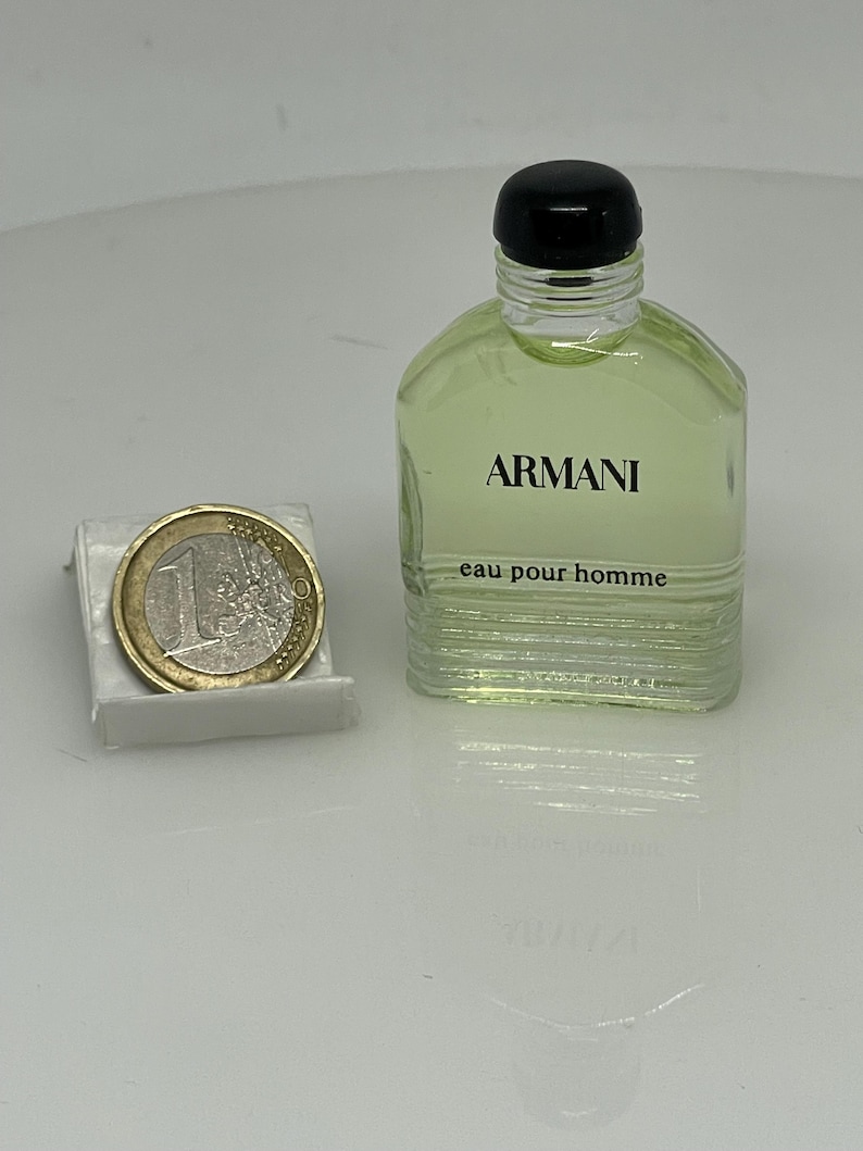 Puede incluir: Un peque&ntilde;o frasco de vidrio transparente de Armani Eau de Toilette para hombre. El frasco tiene una tapa negra y una etiqueta que dice "Armani eau pour homme".