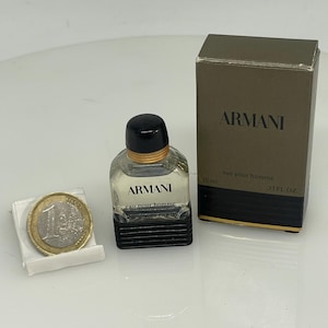 Puede incluir: Un peque&ntilde;o frasco de vidrio transparente de Armani Eau de Toilette para hombre. El frasco tiene una tapa negra y una banda dorada alrededor del cuello. El frasco est&aacute; sobre una superficie blanca junto a una moneda de euro. El frasco est&aacute; etiquetado con "Armani Eau pour Homme" y "10 ml". La caja es marr&oacute;n con letras doradas y dice "Armani Eau pour Homme" y "33 fl oz".