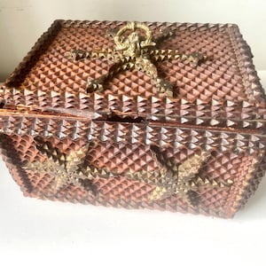 May include: A vintage wooden box with a geometric pattern and brass accents. The box is a reddish-brown color with a repeating diamond pattern carved into the wood. The lid features a decorative brass clasp.