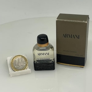Puede incluir: Un peque&ntilde;o frasco de vidrio transparente de Armani Eau de Toilette para hombre. El frasco tiene una tapa negra y una etiqueta negra con las palabras "Armani" y "eau pour homme" impresas en blanco. El frasco est&aacute; al lado de una peque&ntilde;a caja con el mismo dise&ntilde;o y las palabras "Armani" y "eau pour homme" impresas en blanco. La caja tambi&eacute;n tiene las palabras "10 ml" y "33 FL OZ" impresas en ella.