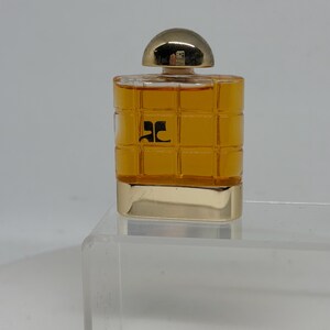Peut inclure: Un petit flacon de parfum rectangulaire avec un bouchon et une base dor&eacute;s. Le flacon est rempli d'un liquide dor&eacute; et porte un logo noir sur le devant. Le design est simple et &eacute;l&eacute;gant, adapt&eacute; &agrave; un parfum.