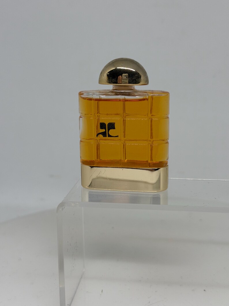 Peut inclure: Un petit flacon de parfum rectangulaire avec un bouchon et une base dor&eacute;s. Le flacon est rempli d'un liquide dor&eacute; et porte un logo noir sur le devant. Le design est simple et &eacute;l&eacute;gant, adapt&eacute; &agrave; un parfum.