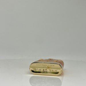 Peut inclure: Un flacon de parfum rectangulaire avec une base dor&eacute;e et un dessus marron clair. Le flacon porte l'inscription "Courr&egrave;ges in blue parfum" et "1/2 Fl.oz 15ml 76% vol Paris".