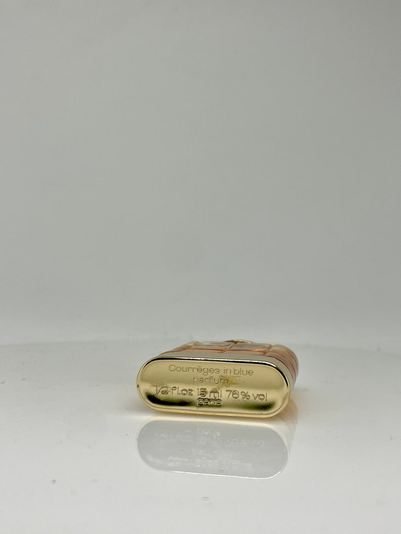 Peut inclure: Un flacon de parfum rectangulaire avec une base dor&eacute;e et un dessus marron clair. Le flacon porte l'inscription "Courr&egrave;ges in blue parfum" et "1/2 Fl.oz 15ml 76% vol Paris".