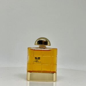 Peut inclure: Un petit flacon de parfum carr&eacute; avec un bouchon et une base dor&eacute;s. La bouteille pr&eacute;sente un motif quadrill&eacute; et contient un liquide de couleur dor&eacute;e. Le logo "ac" est visible sur le devant.