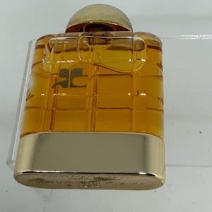 Peut inclure: Petit flacon de parfum rectangulaire avec un bouchon et une base dor&eacute;s. Le corps ambr&eacute; transparent pr&eacute;sente un motif quadrill&eacute;. Le logo "JC" est visible &agrave; l'avant du flacon.