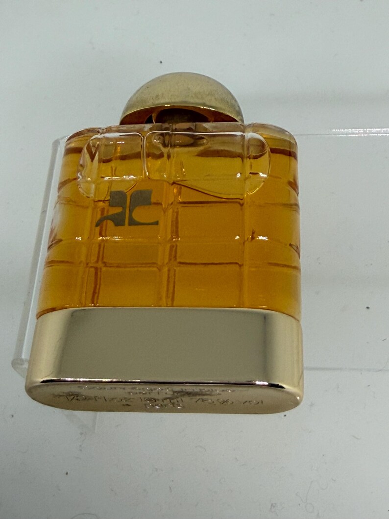 Peut inclure: Petit flacon de parfum rectangulaire avec un bouchon et une base dor&eacute;s. Le corps ambr&eacute; transparent pr&eacute;sente un motif quadrill&eacute;. Le logo "JC" est visible &agrave; l'avant du flacon.