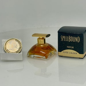 May include: A small bottle of Spellbound perfume by Estée Lauder. The bottle is clear glass with a gold cap and a gold label. The box is black with gold lettering and says "Spellbound Parfum Estée Lauder".