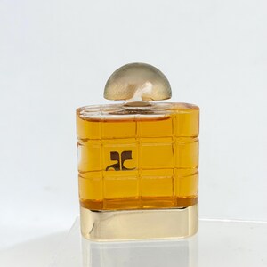 Peut inclure: Un petit flacon de parfum carr&eacute; avec une base dor&eacute;e et un bouchon transparent en forme de d&ocirc;me. Le flacon est de couleur ambre et pr&eacute;sente un motif quadrill&eacute;. Un logo noir est visible &agrave; l'avant.