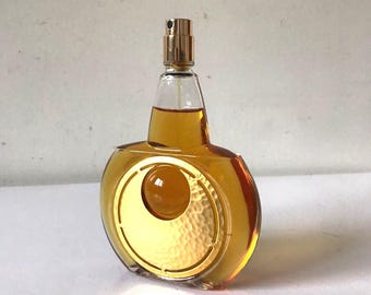Può includere: Un flacone di profumo vintage con tappo color oro e pannello frontale decorativo color oro. La bottiglia è riempita con un liquido color ambra chiaro. La bottiglia ha una forma rotonda con fondo piatto.