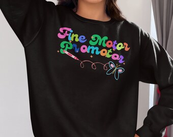 May include: Black sweatshirt with the text "Fine Motor Promoter" in rainbow colours. The text is surrounded by a pink, blue and yellow swirl. A pink crayon and a blue butterfly are also on the sweatshirt.
