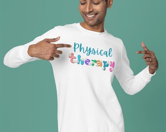 May include: White sweatshirt with the words "Physical Therapy" in teal script with colourful floral accents. The person in the image is pointing at the text. The sweatshirt is paired with white trousers.