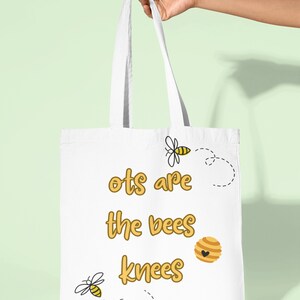 May include: White tote bag with the text "Ots are the bees knees" in yellow lettering. There are two bee illustrations and a honeycomb illustration on the bag.