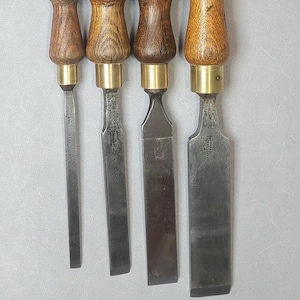 Könnte beinhalten: Fünf Holzmeißel mit Holzgriffen und Messingringen. Die Klingen sind alle unterschiedlich groß und aus Stahl.