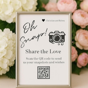 以下が含まれることがあります： 「Oh Snap!」と「Share the Love」の文字が黒字で書かれた額入りのサイン。カメラのグラフィックとQRコードも表示されています。サインは白とピンクの花に囲まれています。