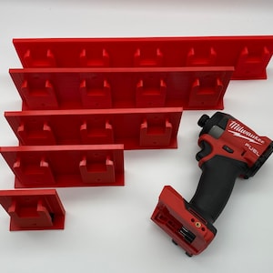 Peut inclure: Organiseurs muraux en plastique rouge avec des fentes pour ranger les outils. Une perceuse Milwaukee FUEL rouge et noire est représentée sur l'image.