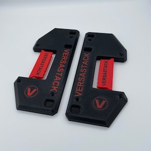 Peut inclure: Deux pièces en plastique noir imprimées en 3D avec le texte "VERSASTACK" imprimé en rouge sur chaque pièce. Les pièces ont un logo V.