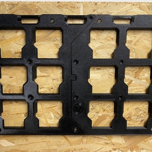 Può includere: Un pannello di stoccaggio rettangolare nero con otto scomparti quadrati. Il pannello è montato su una superficie di legno marrone chiaro. I compartimenti sono progettati per contenere oggetti e il pannello ha diversi fori per viti per il montaggio.