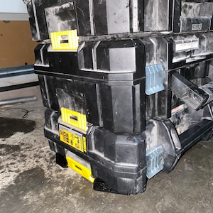 May include: Three black toolboxes stacked on top of each other. The toolboxes have yellow latches and silver clasps. The toolboxes are made of durable plastic.