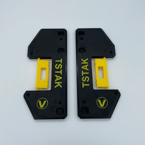 May include: Two black plastic pieces with a yellow insert and the text "Tstak" and a "V" logo.