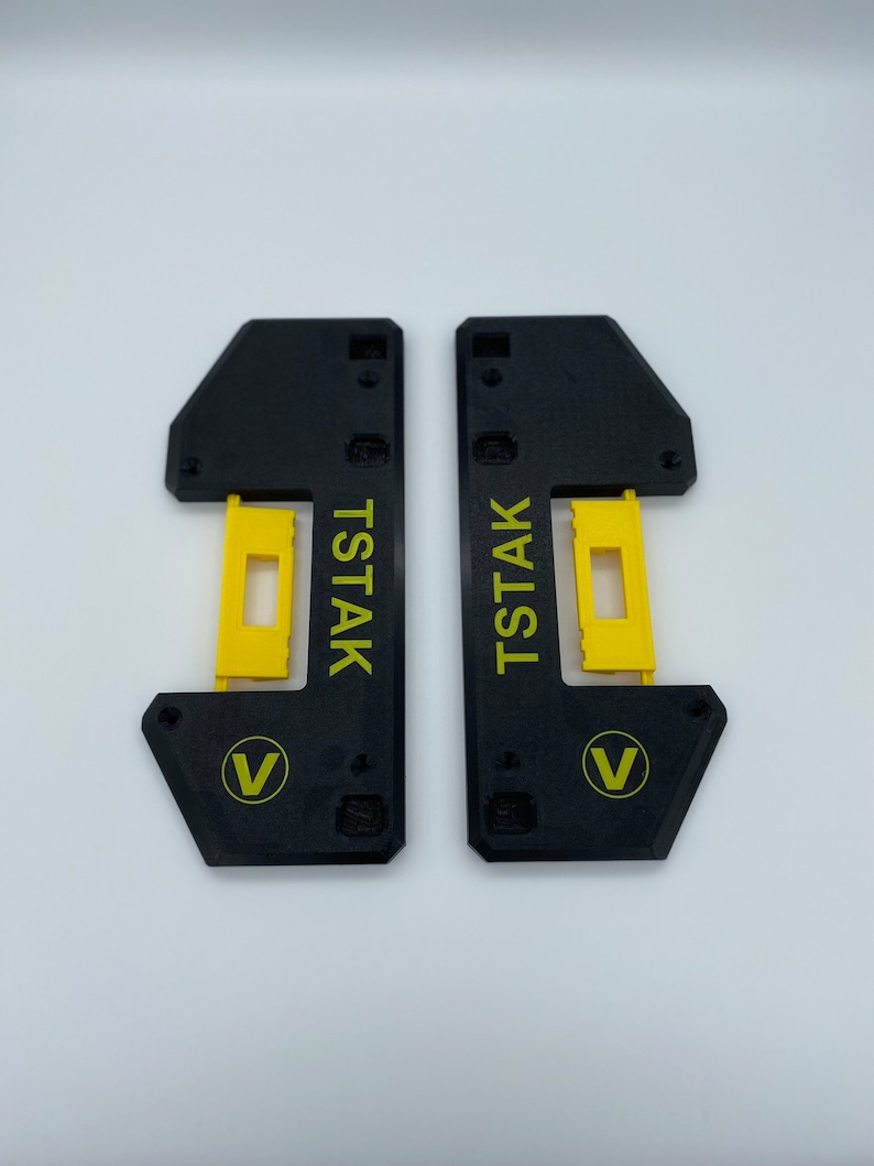 May include: Two black plastic pieces with a yellow insert and the text "Tstak" and a "V" logo.