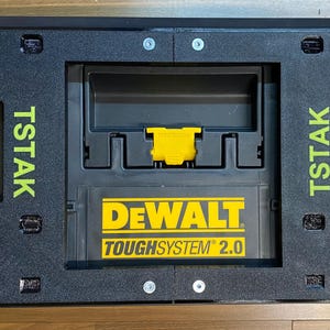Könnte beinhalten: Schwarze und gelbe TSTAK DEWALT TOUGH SYSTEM 2.0 Werkzeugkiste. Die Box hat einen Griff und mehrere Fächer. Das TSTAK-Logo ist grün auf der Seite der Box aufgedruckt. Das DEWALT-Logo ist gelb gedruckt.