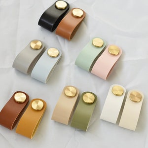 May include: Set of ten leather drawer pulls with brass knobs. The pulls come in a variety of colours, including black, brown, grey, light blue, light green, light pink, beige, and white.