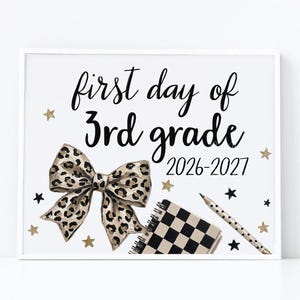 May include: A white sign with black text reading first day of 3rd grade 2026-2027. The design features a large leopard print bow, a black and white chequered notebook, a polka dot pencil, and scattered gold and black stars.