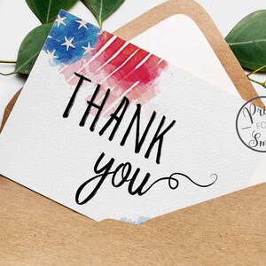 May include: A white card with the words "Thank you" written in black cursive script. The card has a watercolour background with red, white and blue stripes, resembling the American flag. The card is in a brown envelope with a small circle sticker that says "Print for Smile".