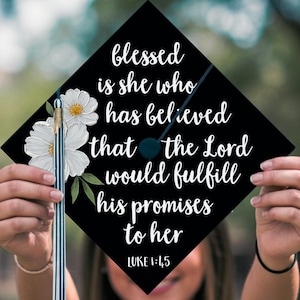 Puede incluir: Un gorro de graduación negro con flores blancas y el texto "blessed is she who has believed that the Lord would fulfill his promises to her" y "LUKE 1:45".