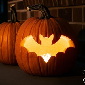 May include: Two orange pumpkins, one with a carved bat design illuminated from within. The pumpkins are set against a dark background, creating a spooky Halloween theme. The words "PRINTABLE STENCIL" are printed vertically on the left side.