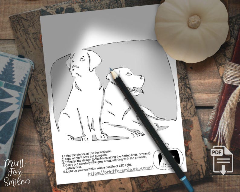 May include: A black and white stencil featuring two Labrador Retrievers, with dotted lines for carving. A pencil rests on the stencil. Instructions are printed below the image, including a website address for the product.
