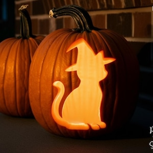 May include: Two orange pumpkins with carved cat silhouettes wearing witch hats. The pumpkins are lit from within, creating a glowing effect. The words "PRINTABLE STENCIL" are printed vertically on the left side of the image.