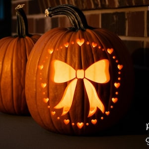 May include: Two orange pumpkins, one with a carved bow and heart design, lit from within. The pumpkins are set against a dark background, with the words "PRINTABLE STENCIL" visible on the left side.