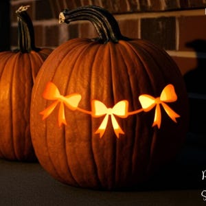 May include: Two orange pumpkins with carved bow designs, illuminated from within. The pumpkins have dark green stems and sit on a dark surface. The image includes the text "PRINTABLE STENCIL" and "Print For Smile".