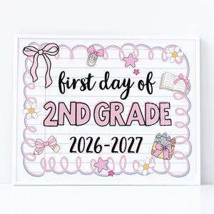 May include: A rectangular sign with a lined paper background featuring the text first day of 2nd Grade 2026-2027. The design includes pink bows, daisies, stars, a paperclip, an open book, and a container of crayons in a pink and blue border.