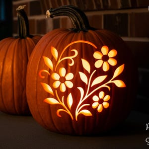 May include: Two orange pumpkins with carved floral designs. The front pumpkin has a detailed flower and leaf pattern, illuminated to create a glowing effect. The text "PRINTABLE STENCIL" is on the left side.