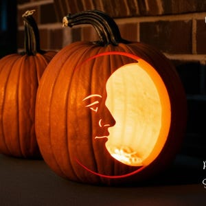 May include: Two orange pumpkins, one with a carved moon face design. The moon face is illuminated from within, creating a warm glow. The words "PRINTABLE STENCIL" are printed vertically on the left side of the image.